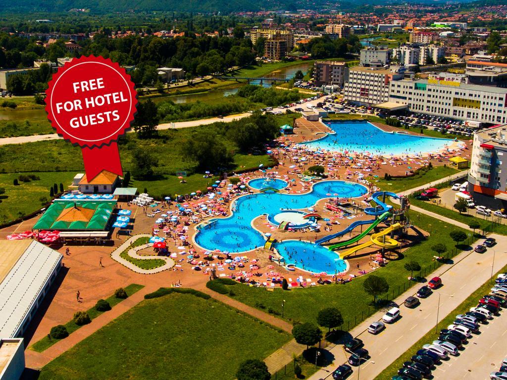 Hotel Hills Sarajevo Congress & Thermal Spa Resort Ilidža Exterior foto The photo shows an aerial view of a large swimming pool area, likely part of a hotel or resort. There are several pools of different shapes and sizes, including one that resembles a Mickey Mouse shape. The area is filled with numerous sun loungers an